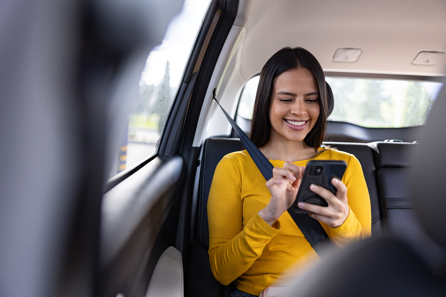 Young woman sitting in the back of a car smiling as she looks down at her mobile phone, csaa specialized services